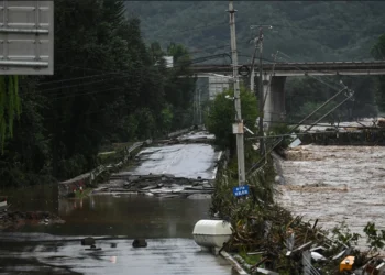 Downed powerlines hang over a buckled road next to high waters following flooding after heavy rains at Xin'anzhuang village, in Miyun district, on the outskirts of Beijing on July 28, 2025. (Photo by Jade GAO / AFP)