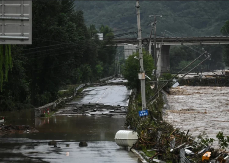 Downed powerlines hang over a buckled road next to high waters following flooding after heavy rains at Xin'anzhuang village, in Miyun district, on the outskirts of Beijing on July 28, 2025. (Photo by Jade GAO / AFP)