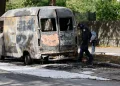 Policemen inspect a torched van close to the burning house