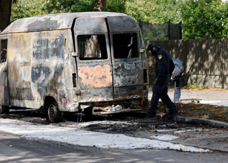 Policemen inspect a torched van close to the burning house