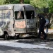 Policemen inspect a torched van close to the burning house