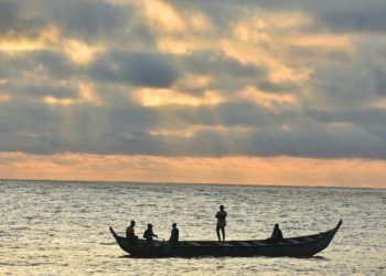A silhouette of fishermen on a canoe at sunset.