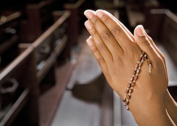 Folded hands in prayer with a rosary resting between the fingers. Image used for representation purposes only