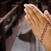 Folded hands in prayer with a rosary resting between the fingers. Image used for representation purposes only